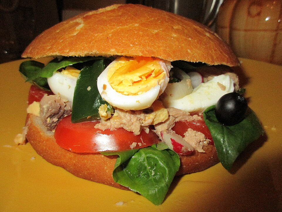 Pan bagnat niçois garni de tomate, œuf, thon, olives et basilic